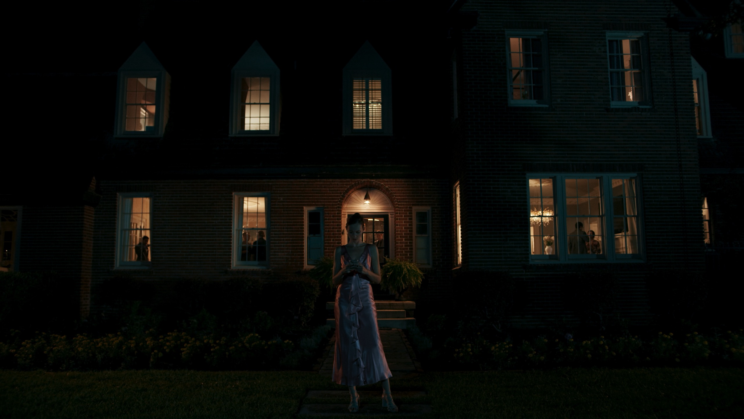Woman alone on lawn in front of warmly lit house at night