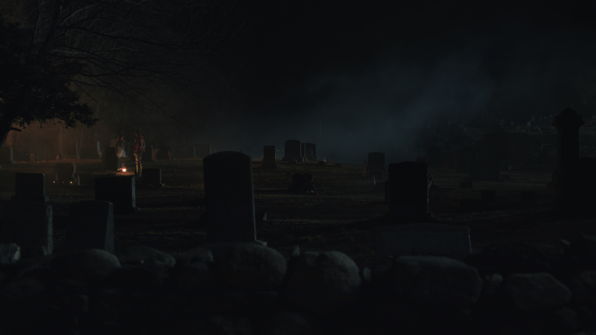 Dark cemetery at night with distant warm glow