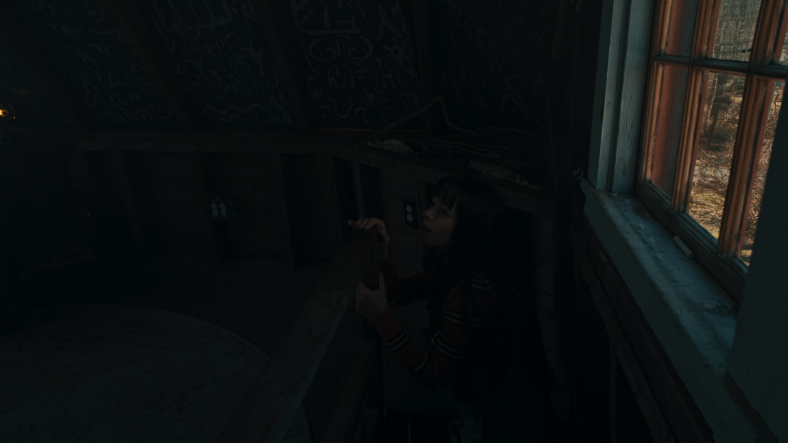 Woman crouched in dark room peering toward window