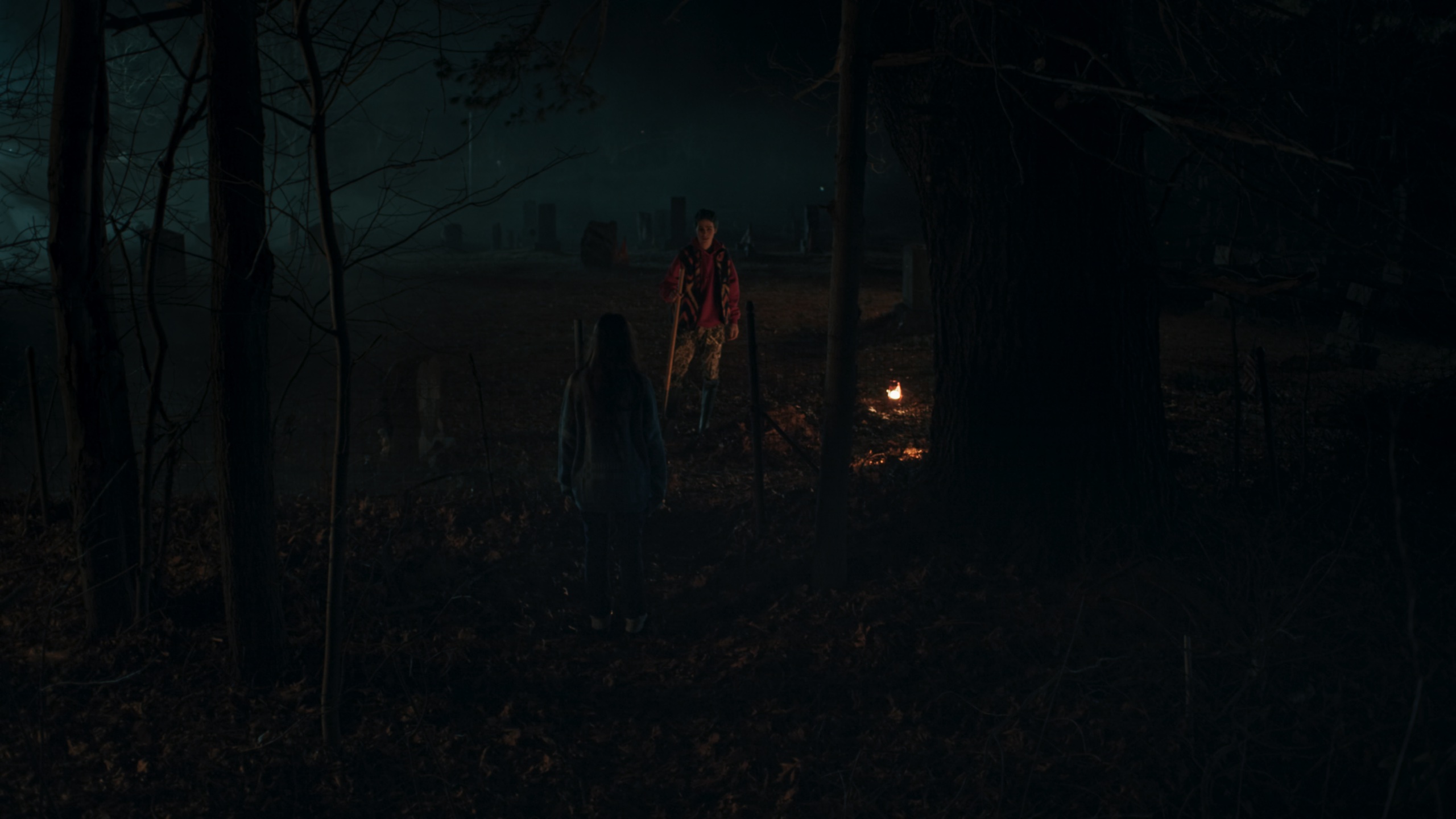 Two figures in dark woods with fire between them