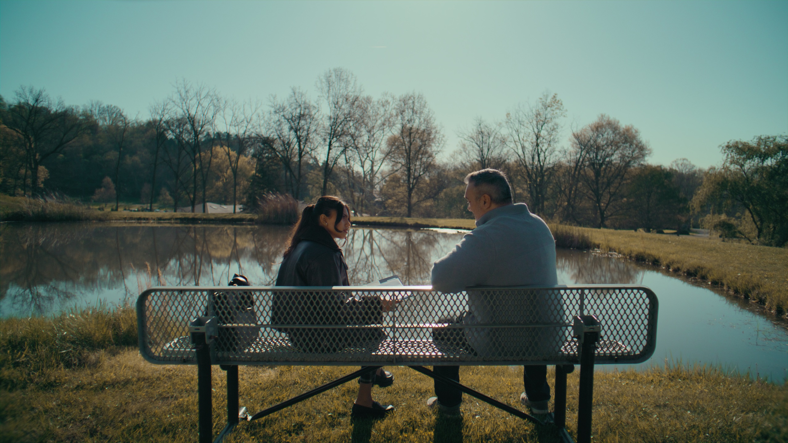 Two figures on park bench overlooking autumn pond