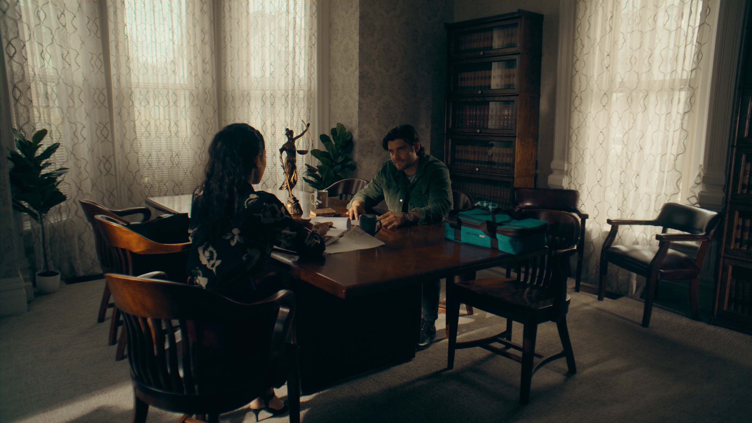 Two figures across desk in office with sheer curtain light
