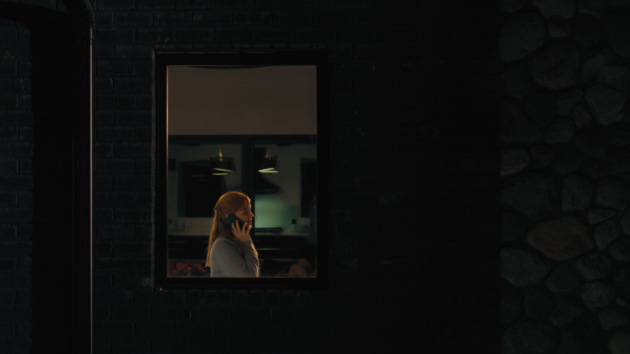 Woman seen through window at night talking on phone